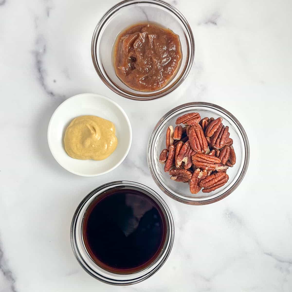 top view close up of the key ingredients for toasted pecan balsamic vinaigrette: date syrup, Dijon mustard, pecans and balsamic vinegar