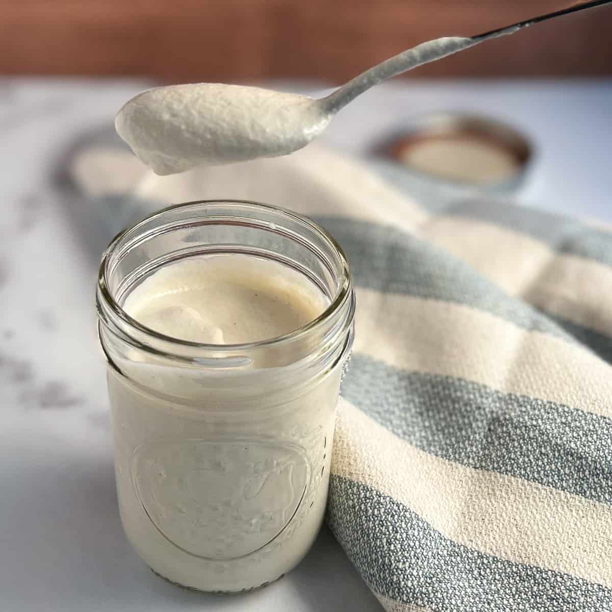 side top view of a mason jar with cashew cream and a spoon dipping some out; blue and white striped napkin on the side