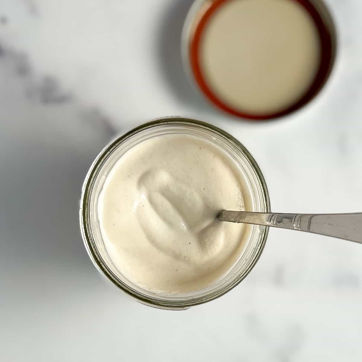 top view close up of vegan sour cream in a mason jar with a spoon sticking out; lid is blurred in the background