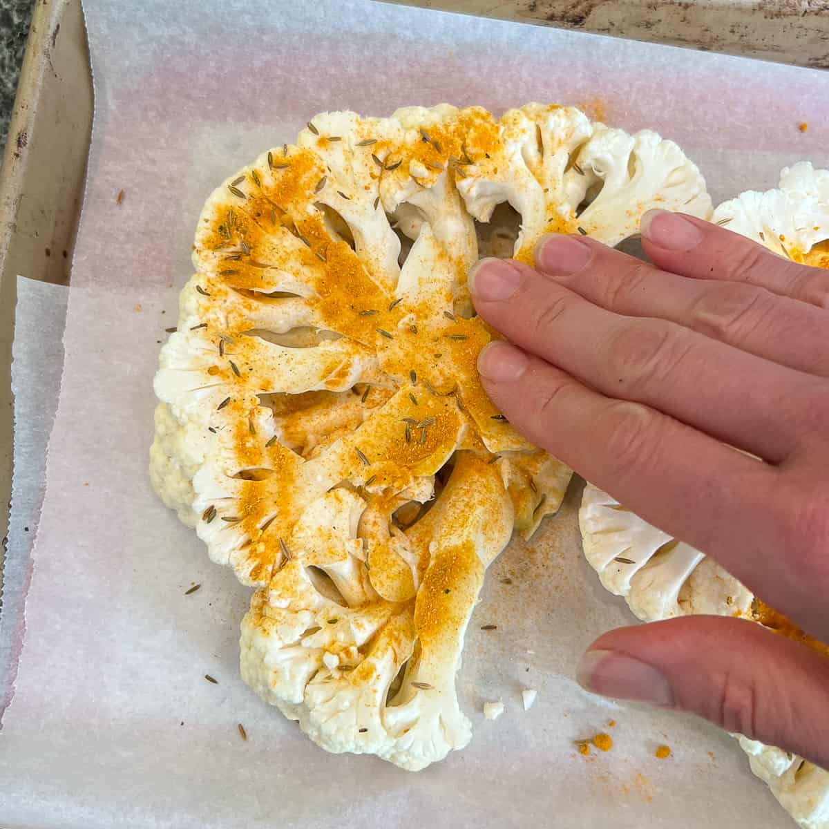 top view of a woman's hand rubbing spice mixture into cauliflower steak