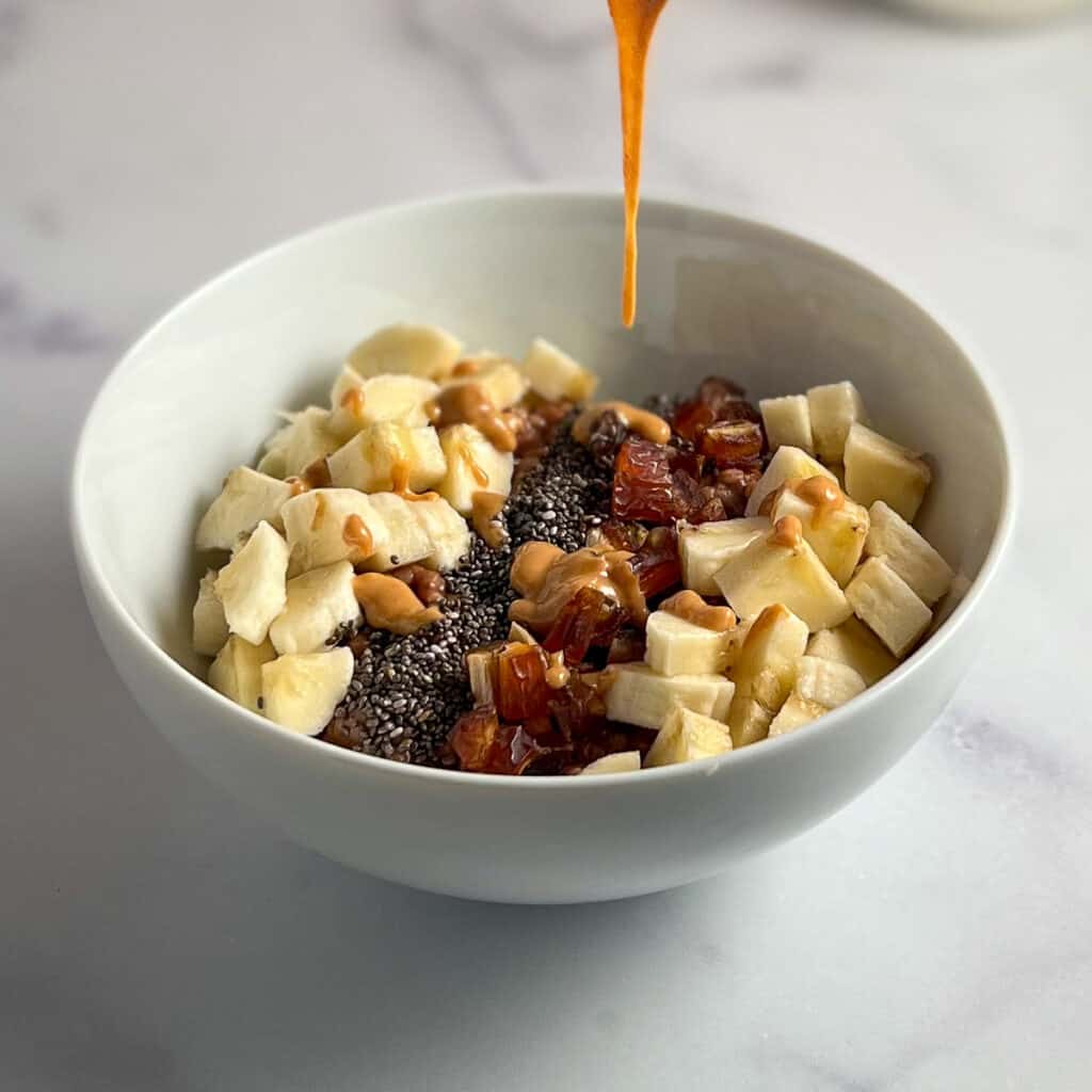 Peanut butter being drizzled on top of a bowl of oatmeal with fruit and chia seeds.