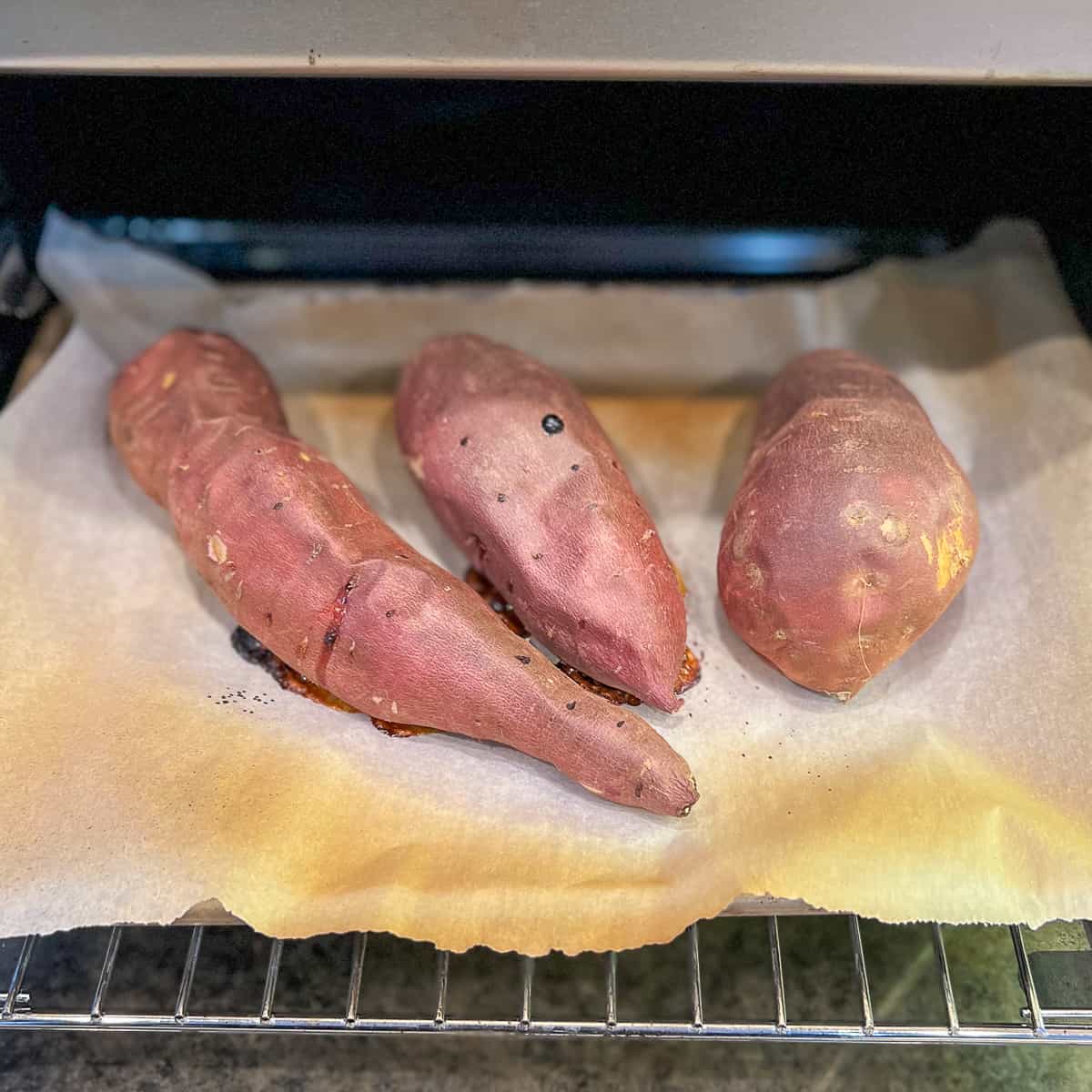 Three baked sweet potatoes on parchment lined baking sheet cooling to room temperature