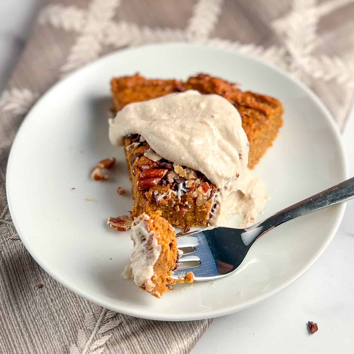 top side view of a slice of crustless sweet potato pie with a dollop of sweet cashew cream and fork with a bite size piece