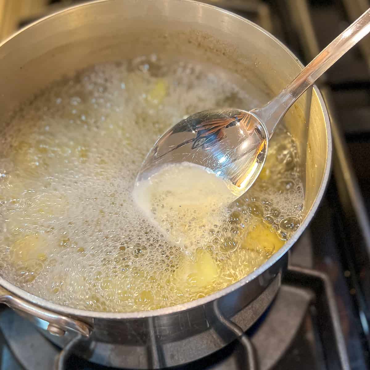 top view of potatoes boiling in a pot; cooking spoon scraping sediment from the top