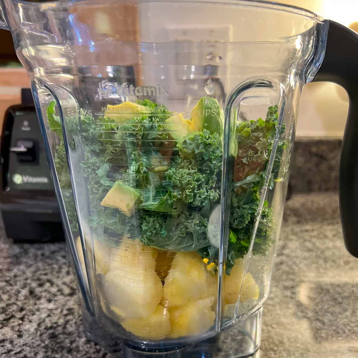 side view of a blender with kale, pineapple and avocado