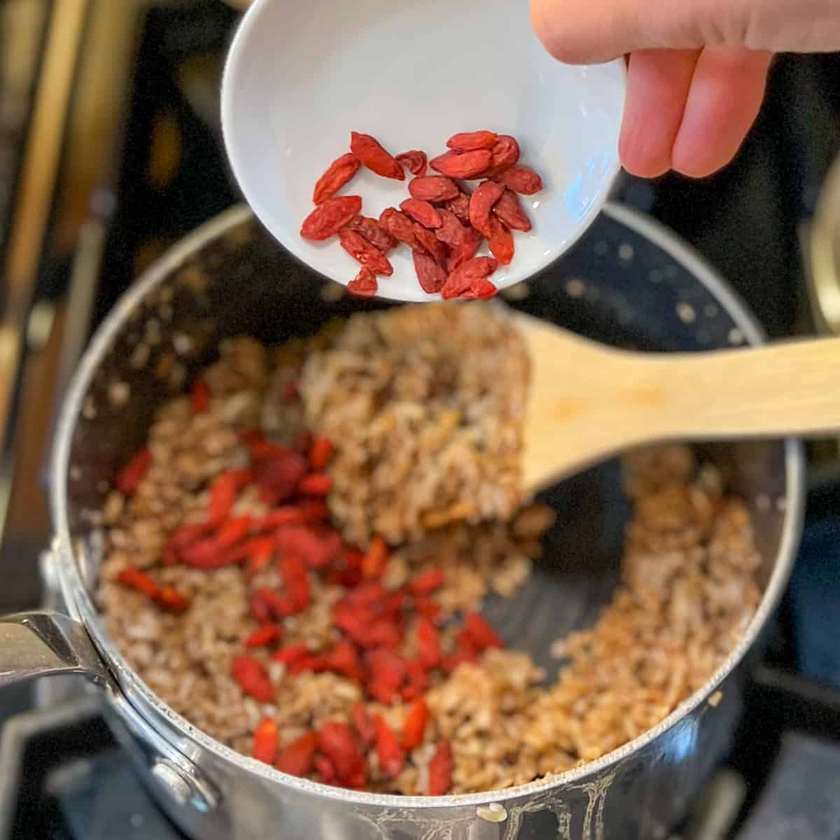 bright red goji berries being added to the pot of cooked oats