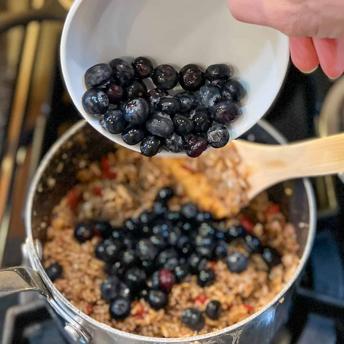 fresh blueberries being added to the pot with cooked oats
