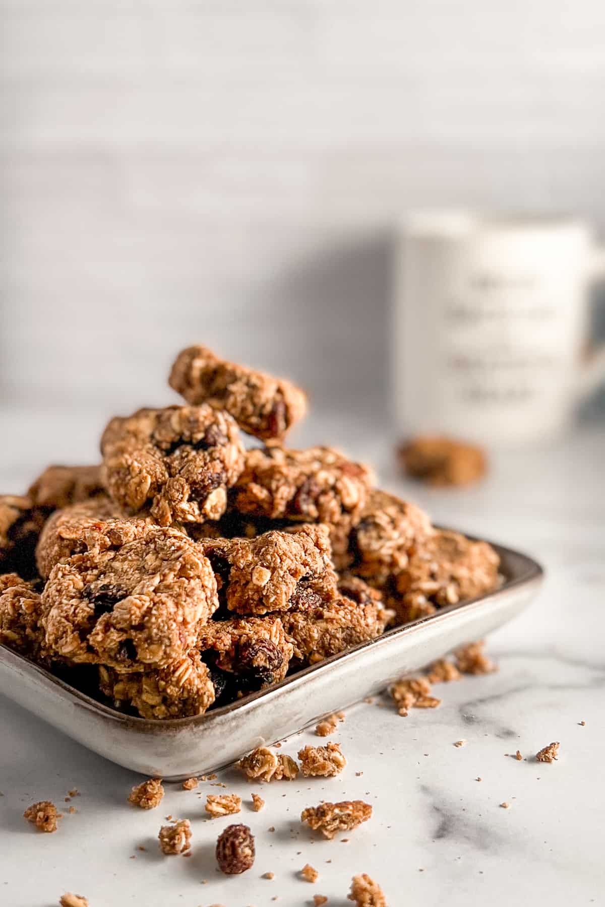Side view and close up stack of healthy oatmeal raisin cookies on a square plate with a mug blurred in the background.