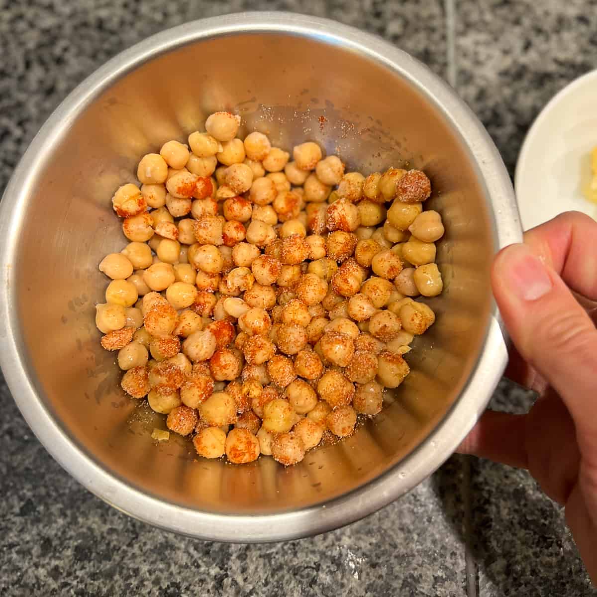 top view of chickpeas being tossed with spices in a mixing bowl