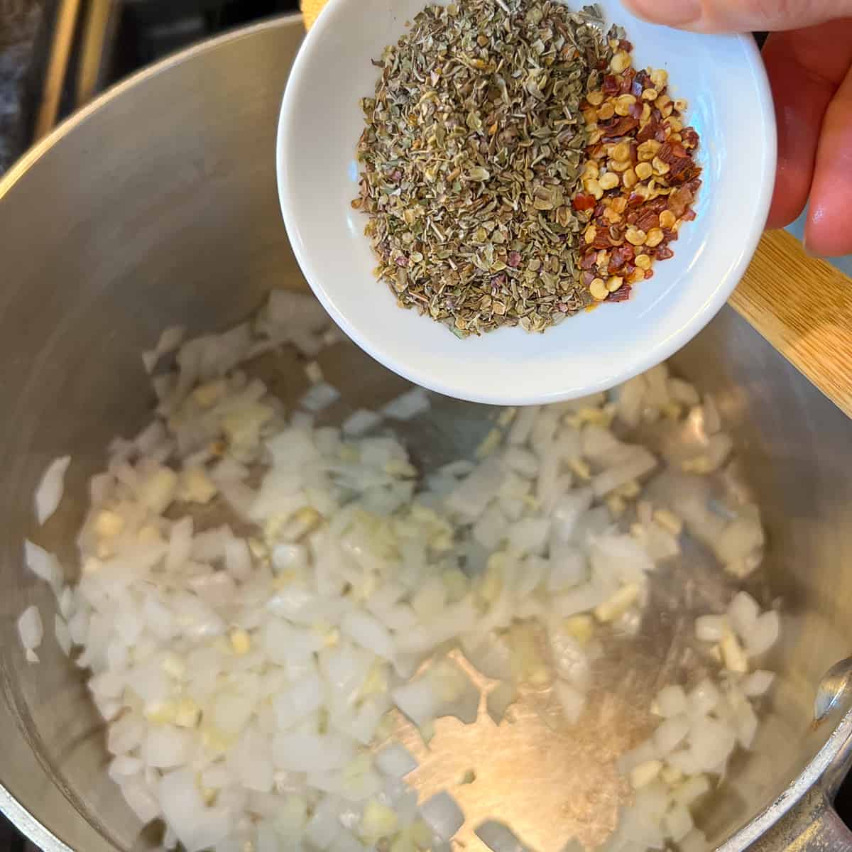 top view of dried spices being added to the pot with onion and garlic
