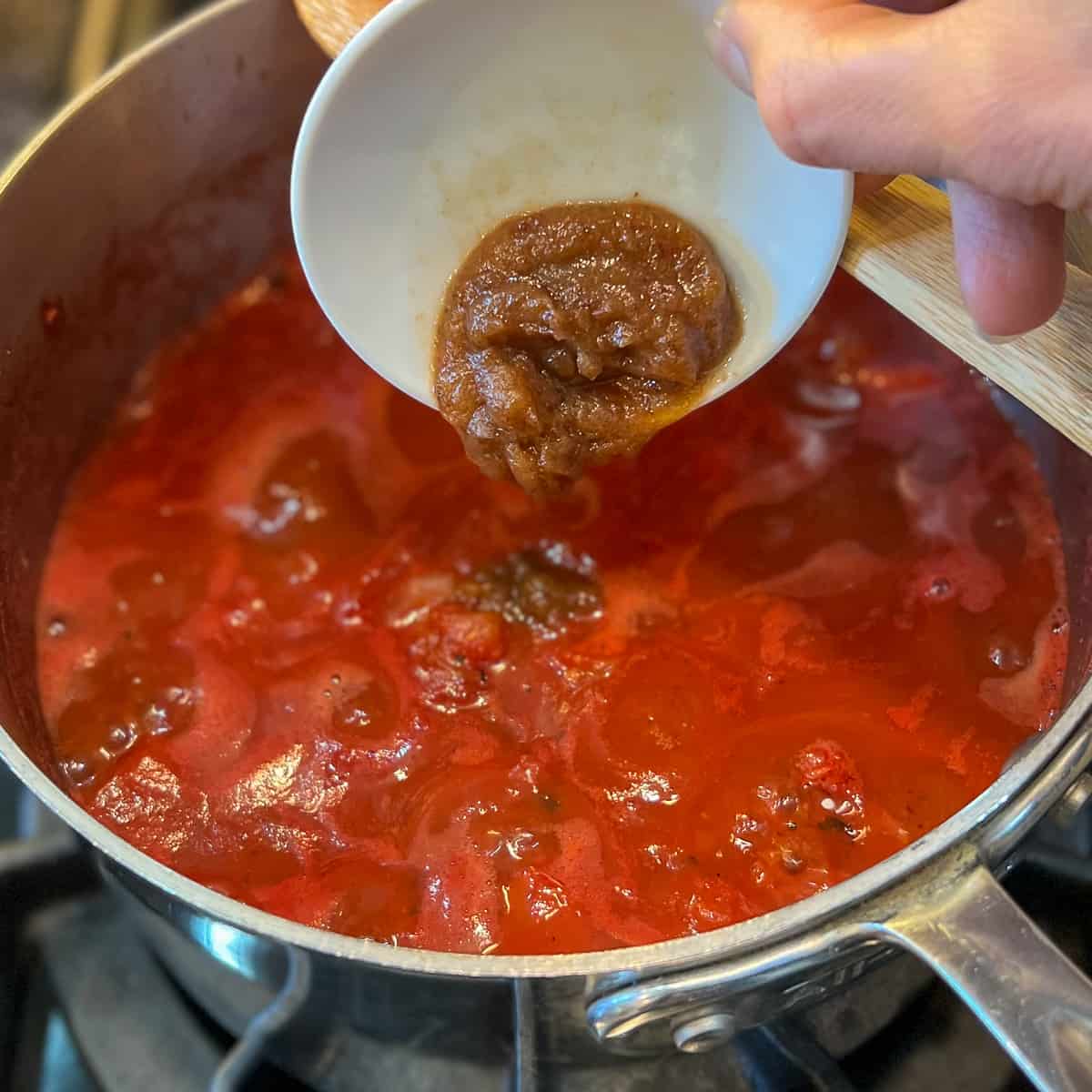 top view of date syrup being added to the simmering marinara sauce