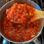 top view close up of a wooden spoon scooping up some marinara sauce from a pot
