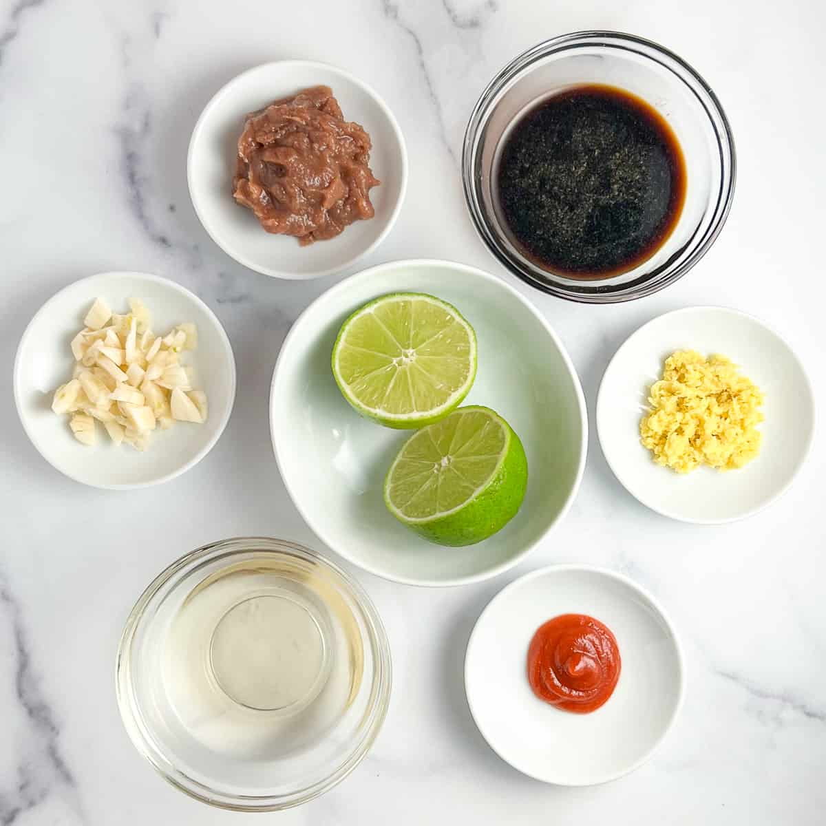 top view of the key ingredients for stir fry sauce: fresh ginger, coconut aminos, simple homemade date syrup, garlic, rice vinegar, sriracha, lime