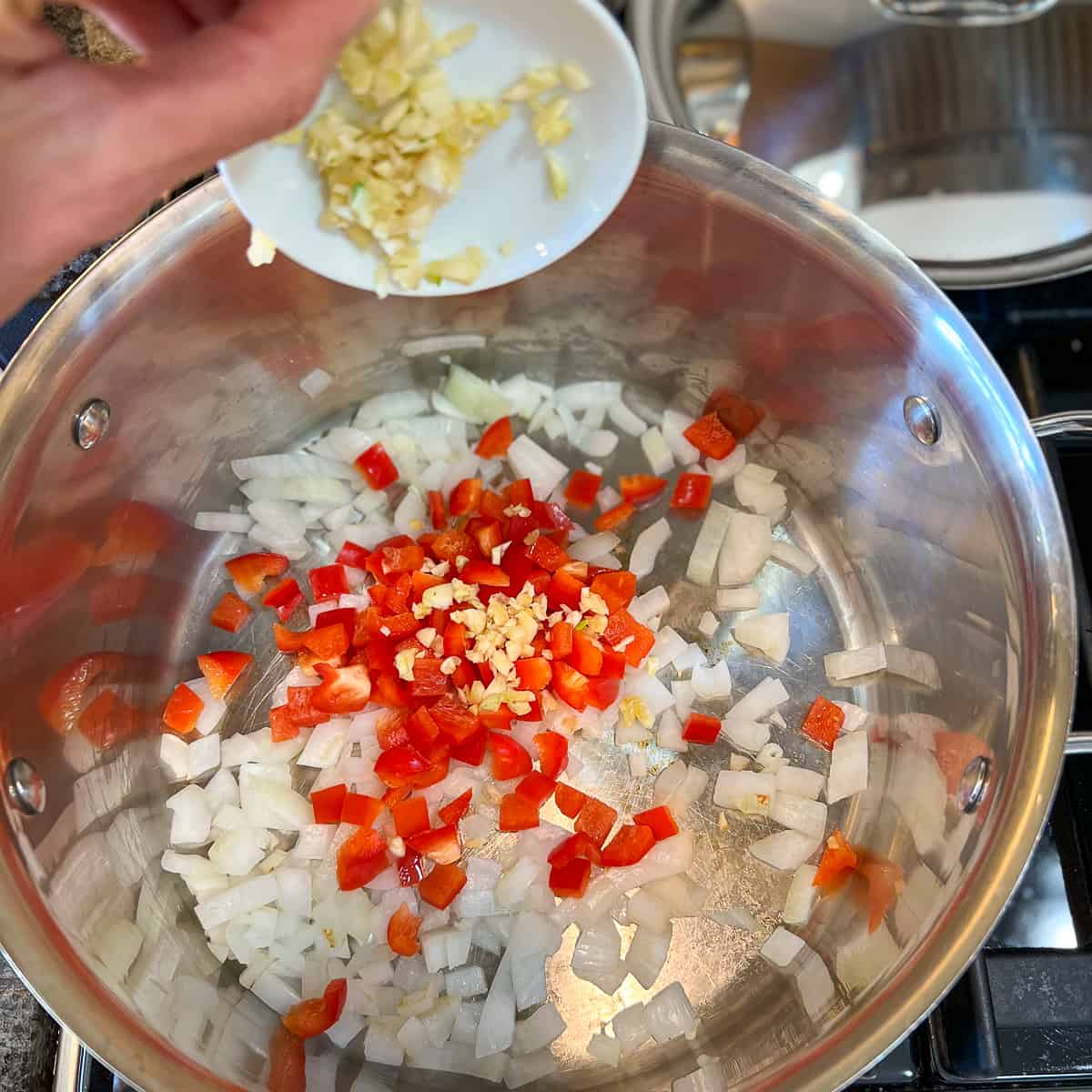 top side view of minced garlic being added to a large pot with chopped onion and red bell pepper