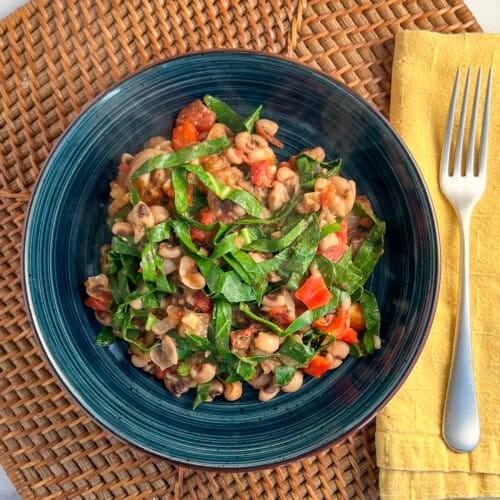 top view of blue plate with black eyed peas and greens with fork and yellow napkin on the side