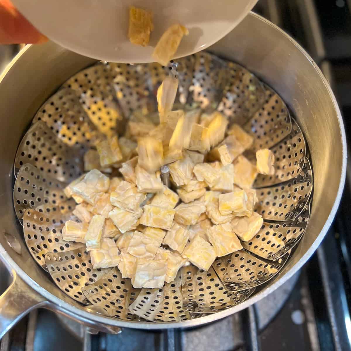top view of cubed tempeh being added to a pot with steamer basket