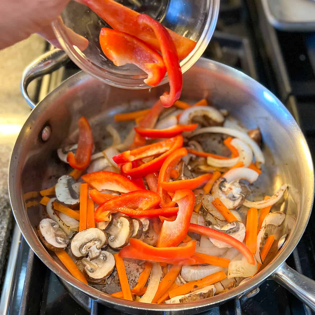 top view of sliced red bell pepper being added to a pan with sautéed veggies