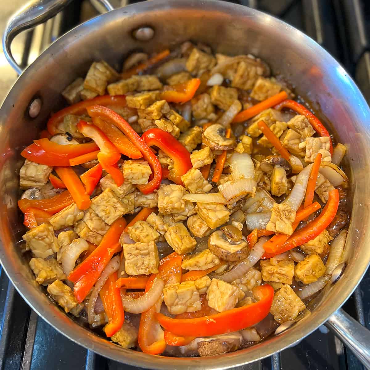 top view of pan on stovetop with tempeh and veggies 