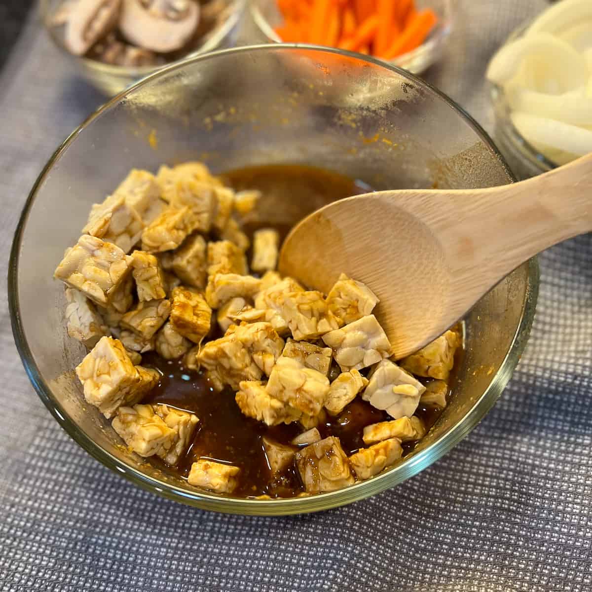 top view of cubed tempeh in marinade sauce and wooden spoon