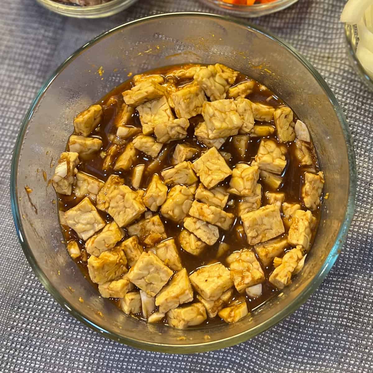 top view of glass bowl with tempeh being marinated in brown sauce