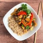 top view of stir fry with brown rice in a rounded square white bowl and wooden chopsticks on the side