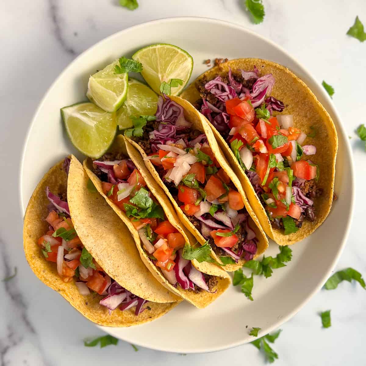 top view close up of four vegan black bean tacos topped with fresh pico de gallo and shredded cabbage