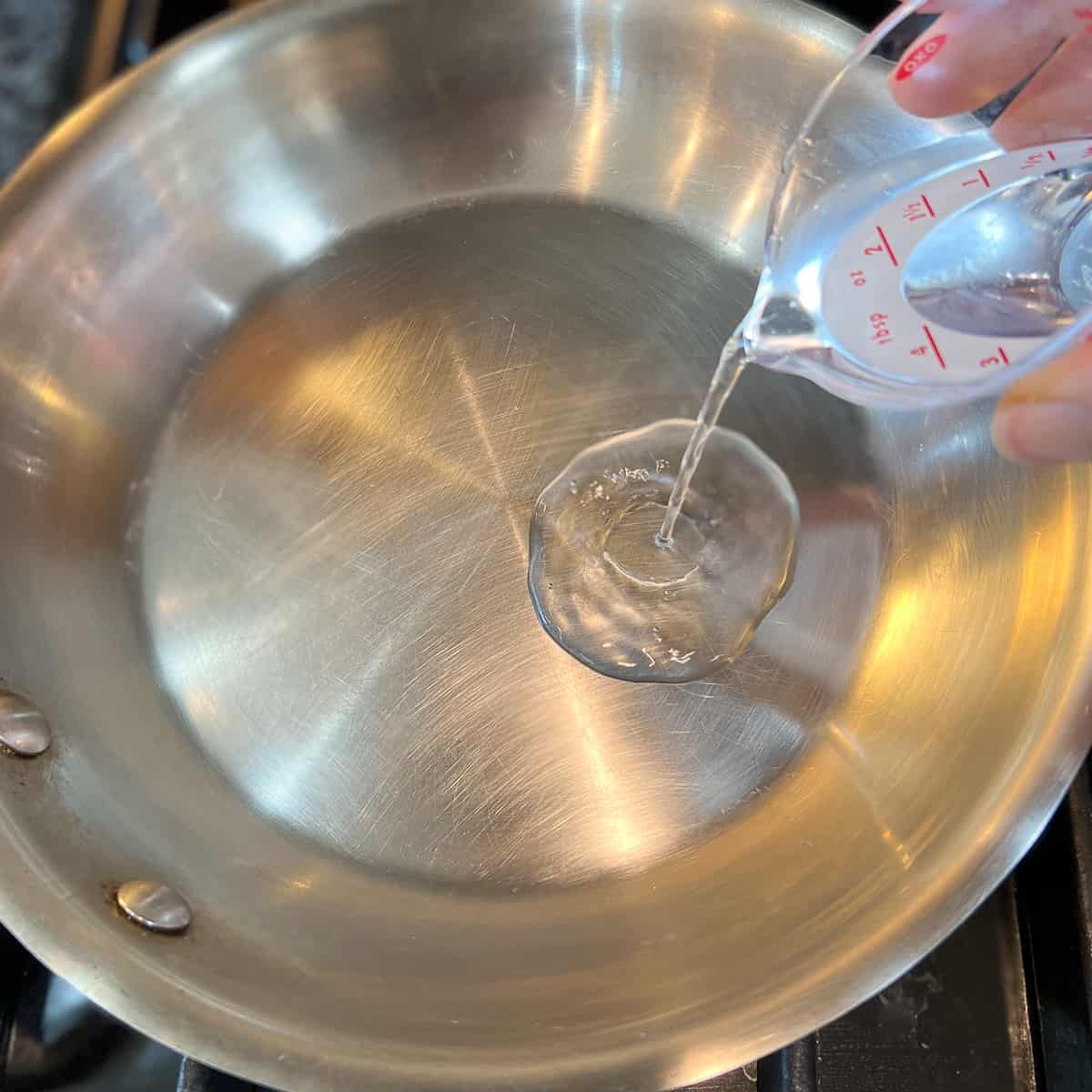 top view of stainless skillet and water being poured into it