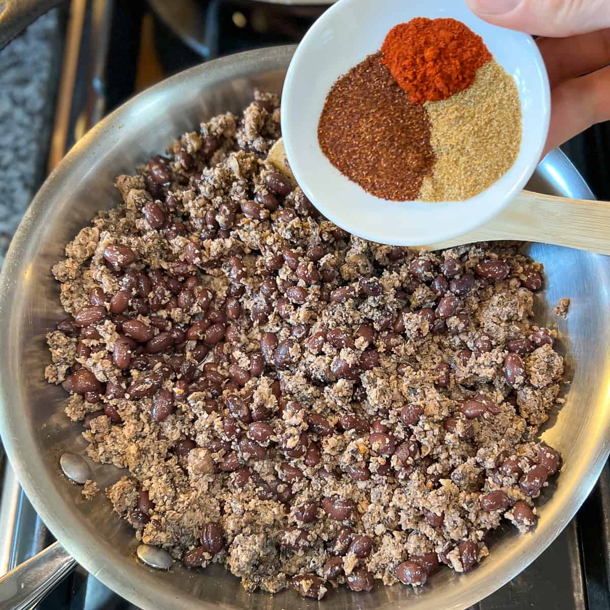 top view of vegan taco meat in the skillet with three spices being added to it