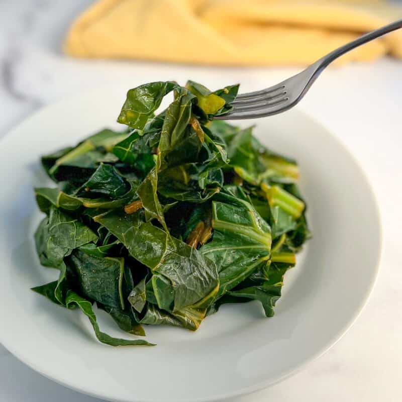 side view close up of cooked vegan collard greens on a white plate with fork