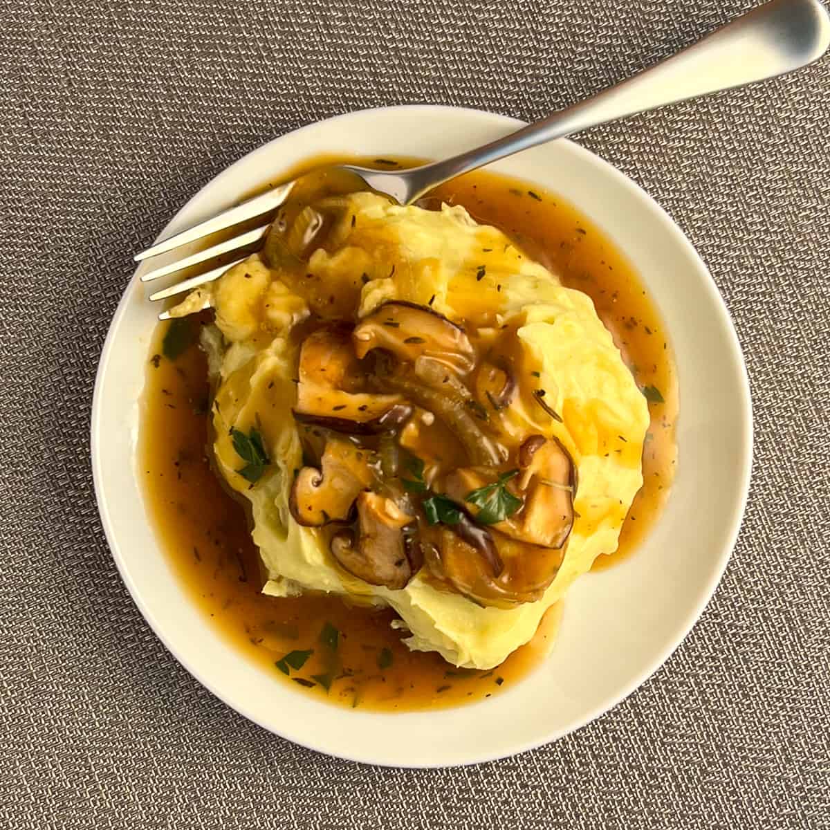 top view of vegan mushroom gravy on a white plate of mashed potatoes with fork on the side