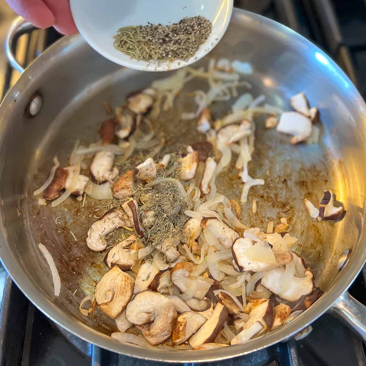 spices being added to a pan with mushrooms and onions