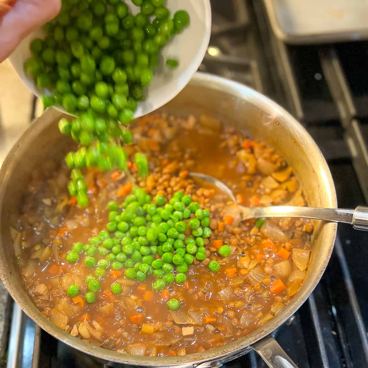 green peas being added to the cooked lentils and veggies