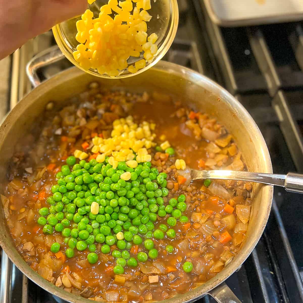 corn being added to the lentil and veggie mixture in the large pan