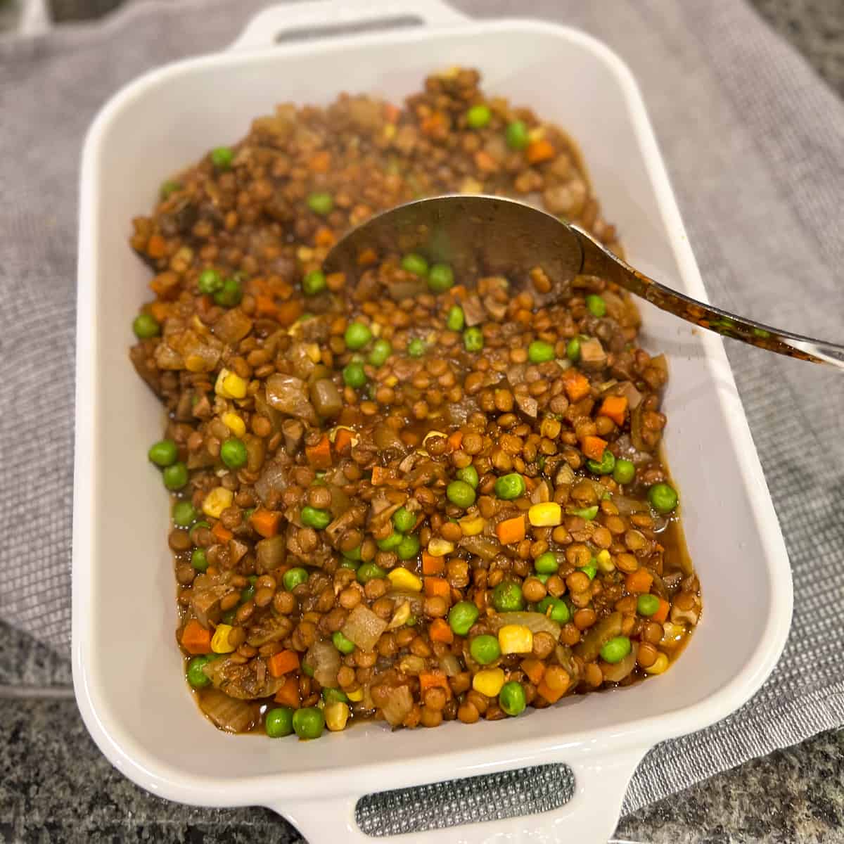 top side view of lentil and veggie mixture in a white rectangular casserole dish with large cooking spoon