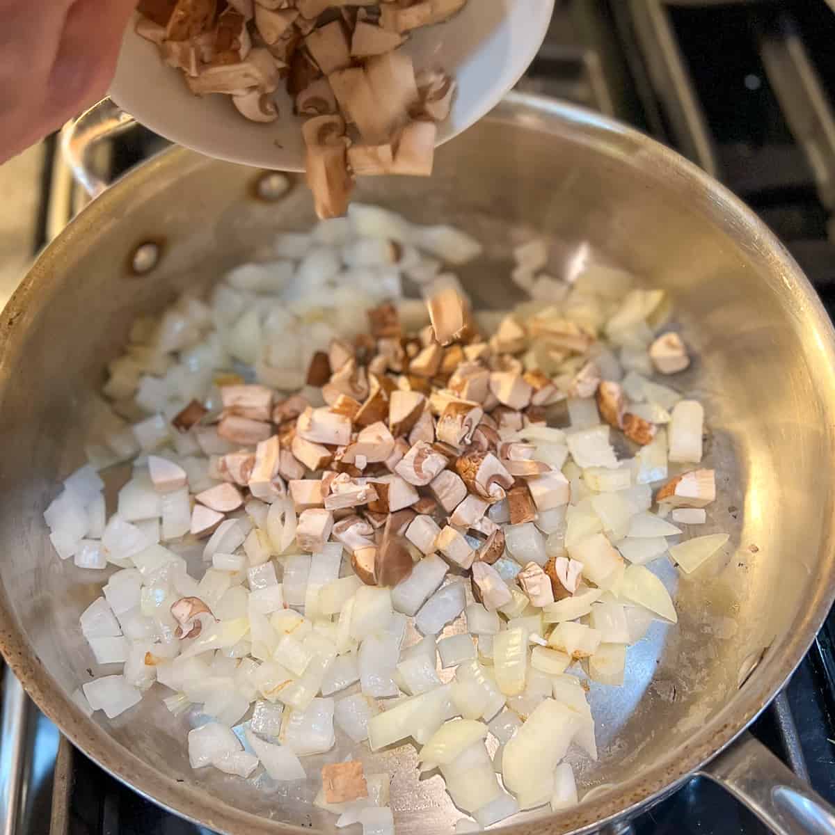 top side view of diced mushrooms being added to pan with chopped onion