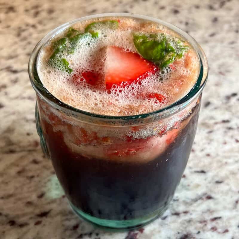 top side close up of a mocktail with fresh strawberries, basil and balsamic vinegar on a granite countertop