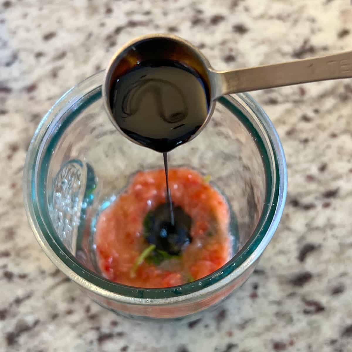 top view of balsamic vinegar being poured into the glass with muddled strawberry and basil