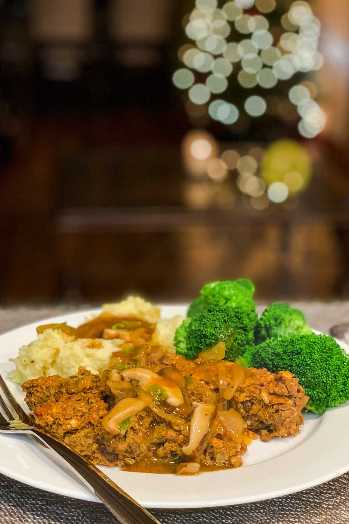 side view of lentil quinoa loaf (vegan, gluten free, oil free), garlic mashed potatoes with caramelized onion and mushroom gravy and a side of steamed broccoli on a white plate