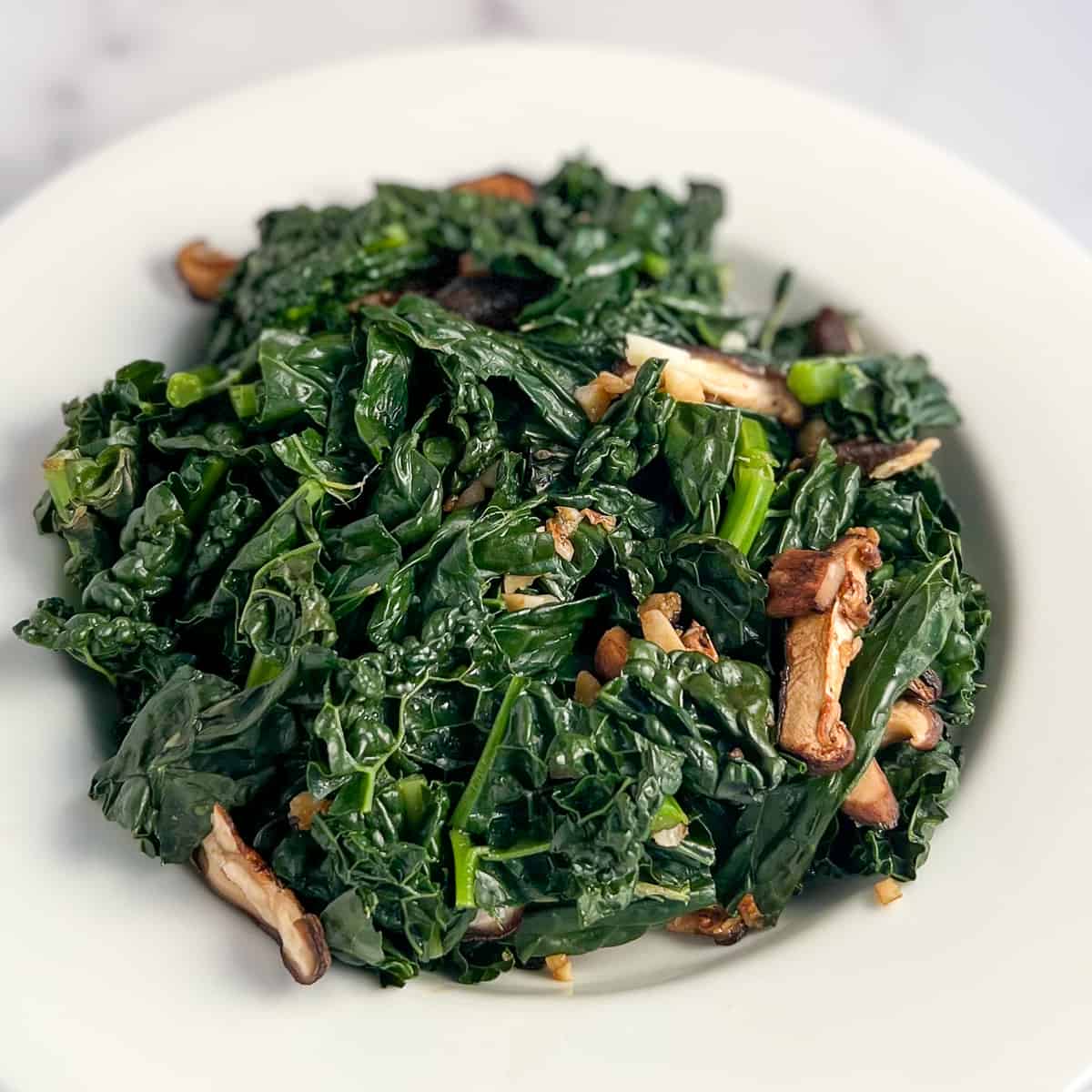 top side view of sauteed kale and mushrooms in a white rimmed bowl