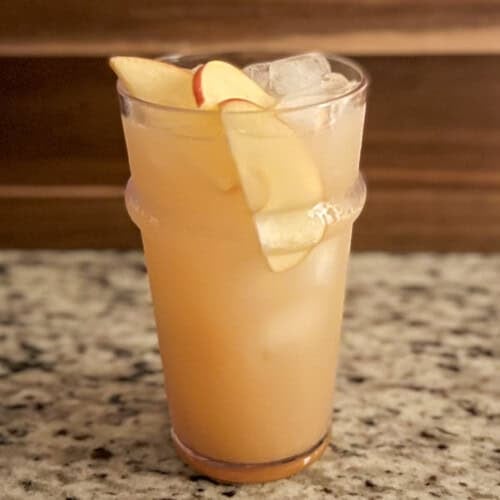 side view close up of apple cider mocktail in a tall glass with ice and sliced apple