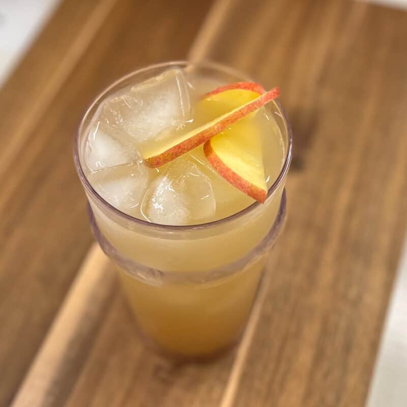 top side view of ginger spiced apple cider spritzer on ice with sliced apples on top; this mocktail is sitting on a wooden board