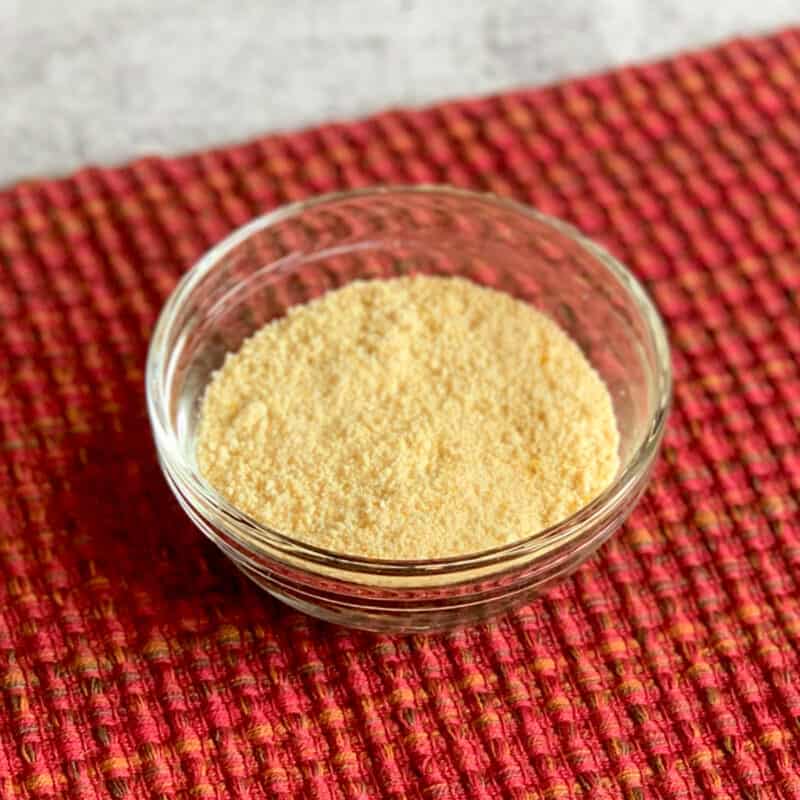 top side view of vegan parmesan cheese in a clear glass dish sitting on a red woven placemat