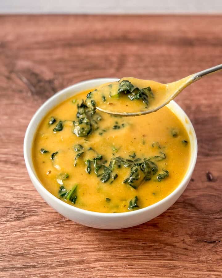 A bowl of white bean and kale soup with a spoon lifting some out of the bowl.
