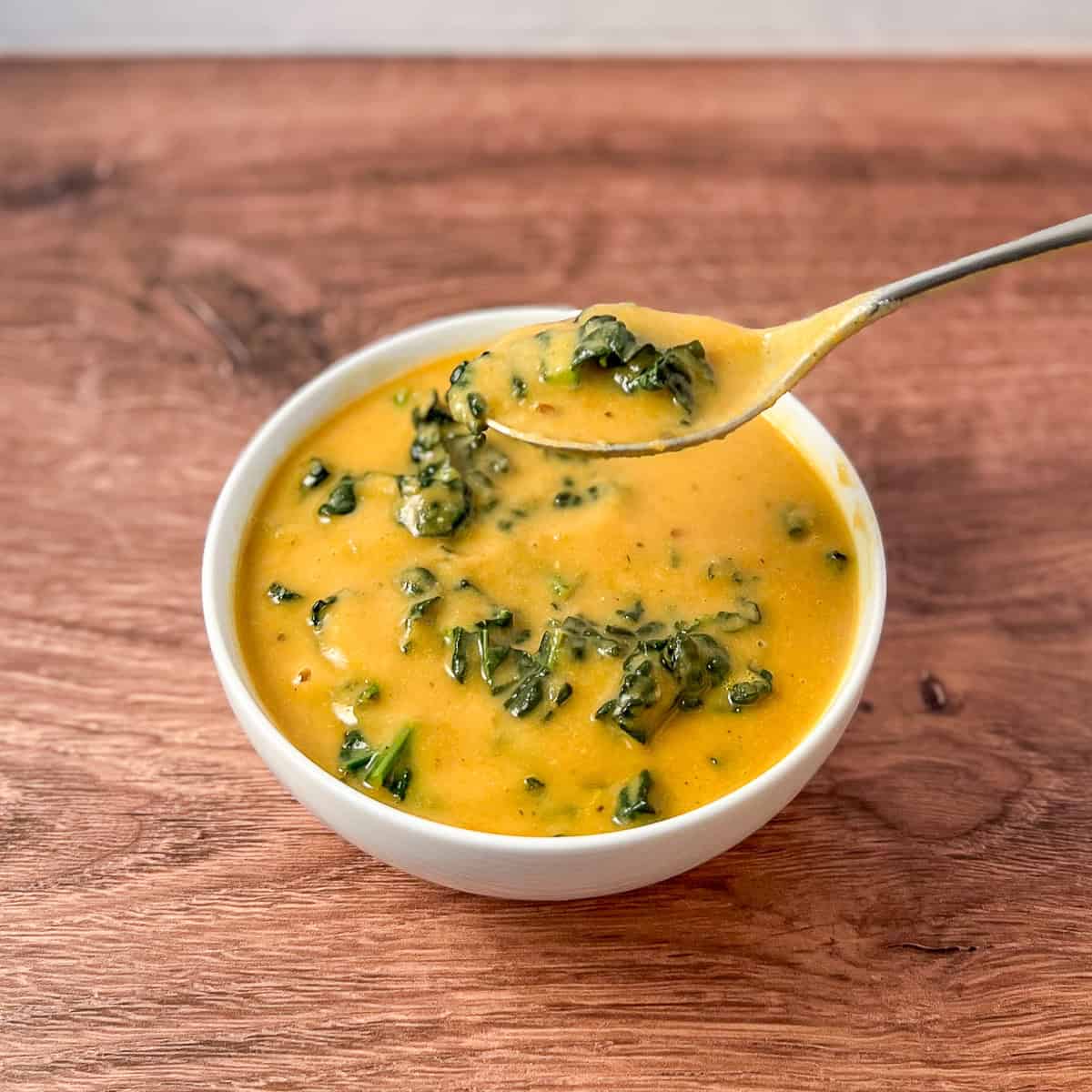 A bowl of white bean and kale soup with a spoon lifting some out of the bowl.