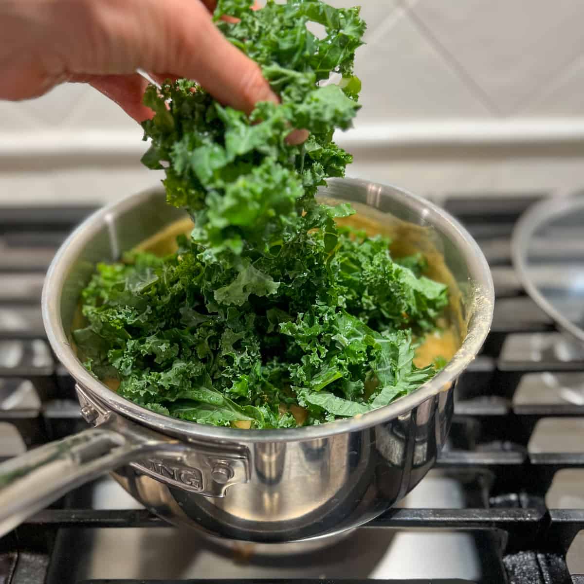 top side view of fresh chopped kale being added to the soup mixture in the pot on the stovetop