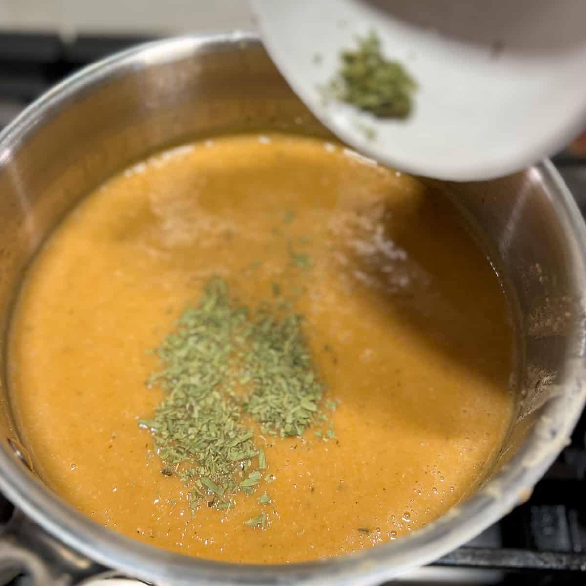top side view of dried tarragon being added to the soup mixture in the pot on the stovetop