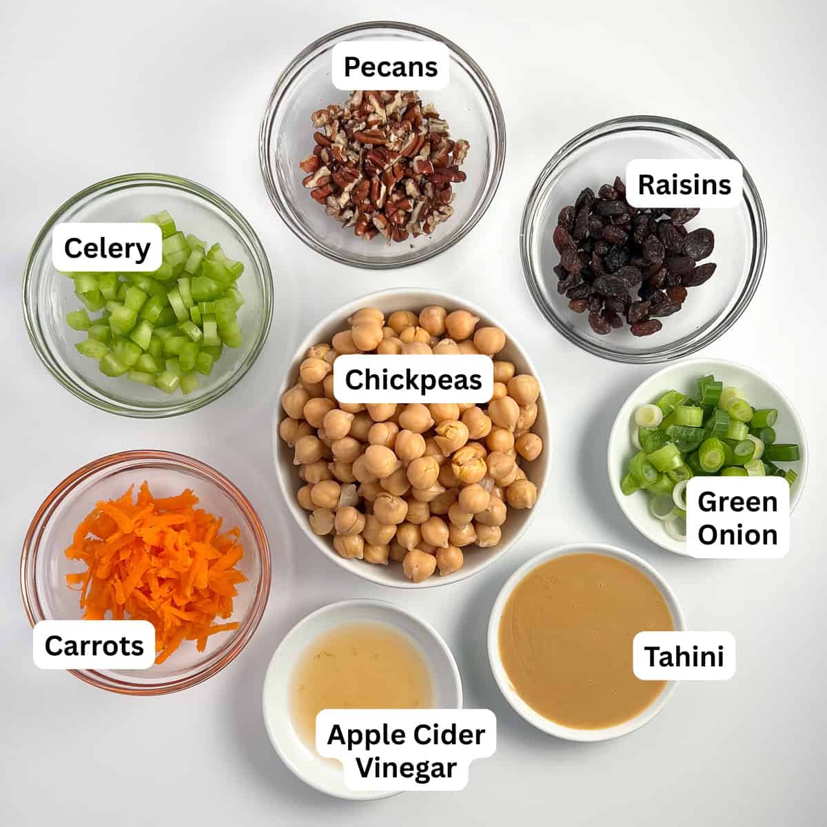 Ingredients for vegan chickpea salad: chickpeas, celery, raisins, green onion, shredded carrot, chopped pecans, tahini, apple cider vinegar.