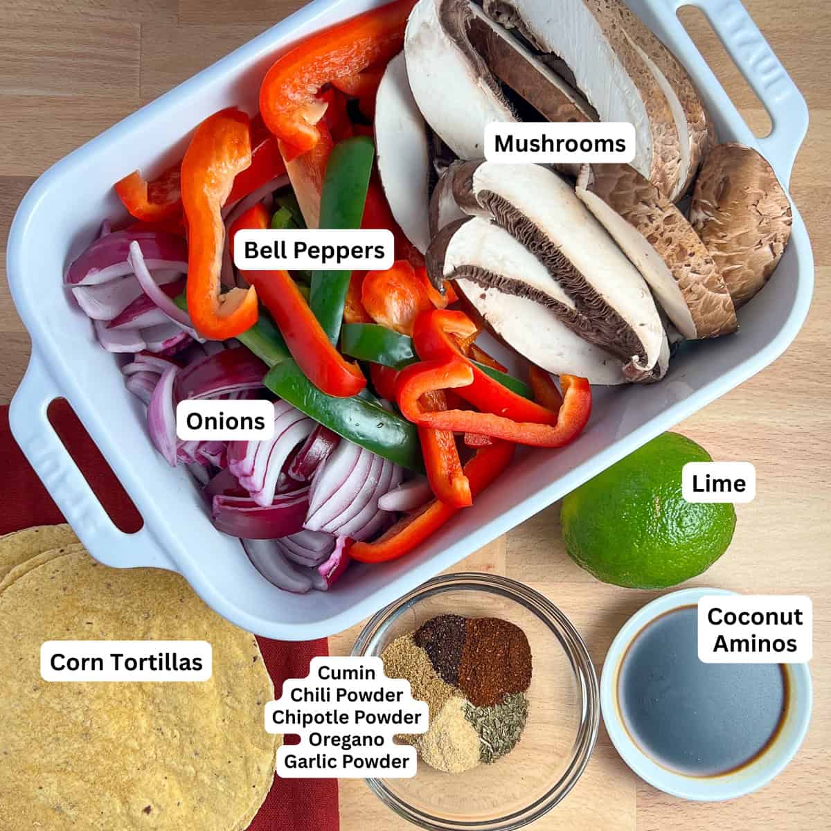 Ingredients for vegan fajitas: sliced mushrooms, bell pepper, and onion, spices, lime, coconut aminos and corn tortillas.