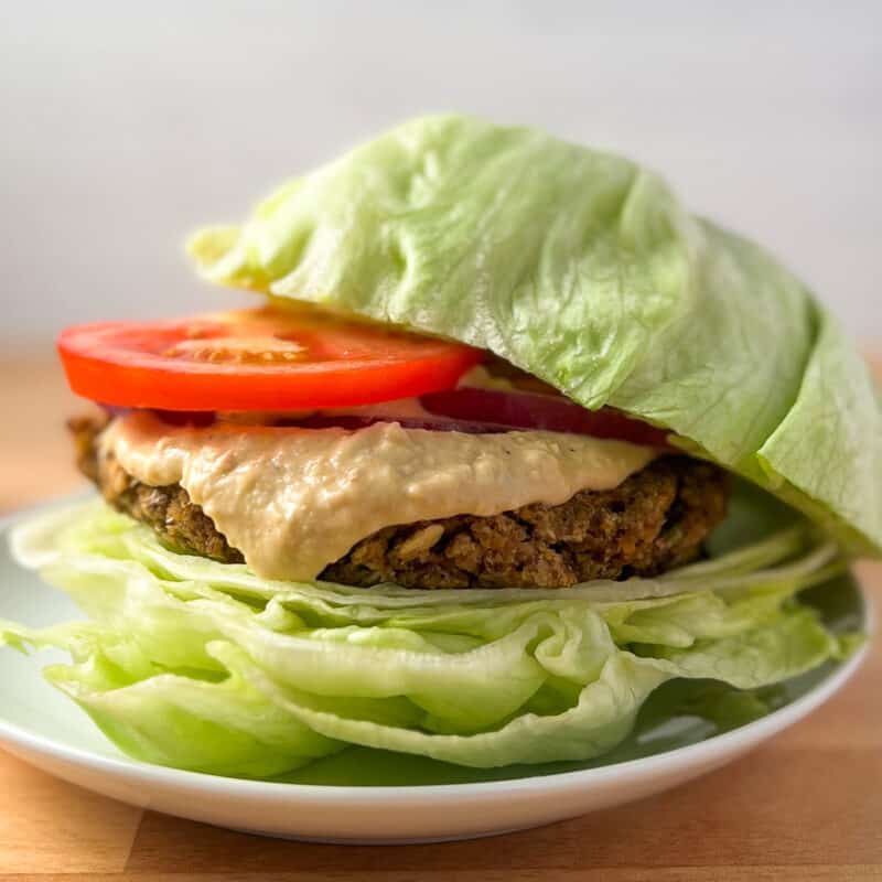 side view close up of chickpea burger on lettuce bun with sliced tomato, onion and hummus sauce