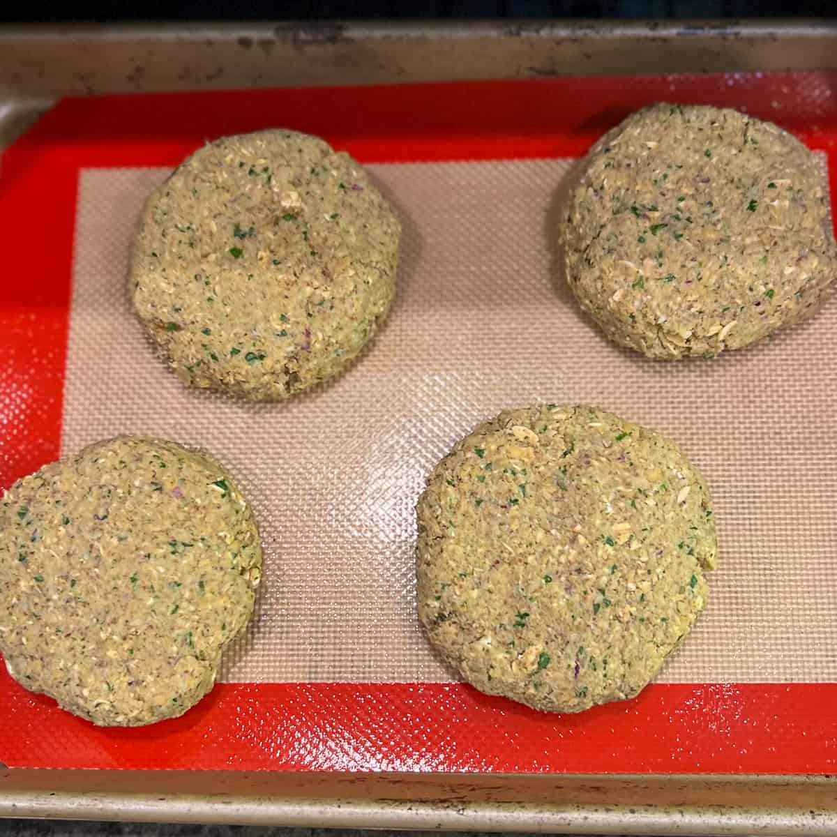 top view of four chickpea patty burgers on a silicone-lined mat in a baking sheet